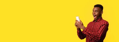 Mobil Teklif. Zeki telefon ekranına heyecanla bakan komik siyah adam, çevrimiçi haberlere duygusal tepki veren, ağzı açık duran, sarı arka planda izole edilmiş, boşluğu kopyalayan.