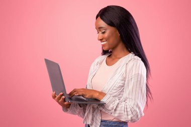 Milenyum Afrikalı Amerikalı kadın dizüstü bilgisayarla çalışıyor, pembe stüdyo geçmişi üzerinde çalışıyor ya da çalışıyor. İnternette iletişim kuran, film ya da video izleyen güzel siyahi kadın.