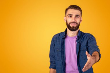 Selamlama konsepti. Turuncu stüdyo arka planında elini sıkmak için elini uzatan gülümseyen beyaz adam. Olumlu genç adam anlaşma yapıyor, ortaklık ya da arkadaşlık teklif ediyor.