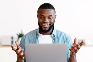 Web Konferansı. Milenyum Afrikalı Amerikalı neşeli bir adam dizüstü bilgisayarında video görüşmesi yapıyor, sırasına oturmuş bilgisayarla gülümseyen, kameraya el sallayan ve internetten haberleşmenin tadını çıkaran siyah bir adam.