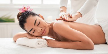 Sırt masajı. Güzel Asyalı kadın spa salonunda profesyonel masör tarafından tedavi ediliyor, rahat Koreli kadın güzellik ve sağlık gününün tadını çıkarıyor, kapalı gözlerle yatıyor, boş alanla yakın çekim yapıyor.