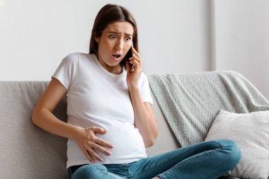 İşçi Partisi. Endişeli hamile kadın doktora sesleniyor, koltukta otururken karnına kramplar giriyor, hamile kadın akut karın ağrısı ve kasılmalarından muzdarip,