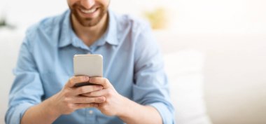 Mutlu Sakallı Adam akıllı telefon mesajları kullanıyor ve cep telefonu uygulamasını evdeki koltukta otururken kullanıyor. Harika uygulama, cep telefonu kullanan adam interneti tarıyor ya da kapalı alanda oyun oynuyor. Sığ Derinlik