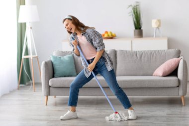 Evdeki yerleri silerken şarkı söyleyen, mikrofon olarak paspası kullanan, ev işlerinde eğlenen güzel bir kadın. Ev işlerinden hoşlanan neşeli genç bir kadın, mesaj için yer.