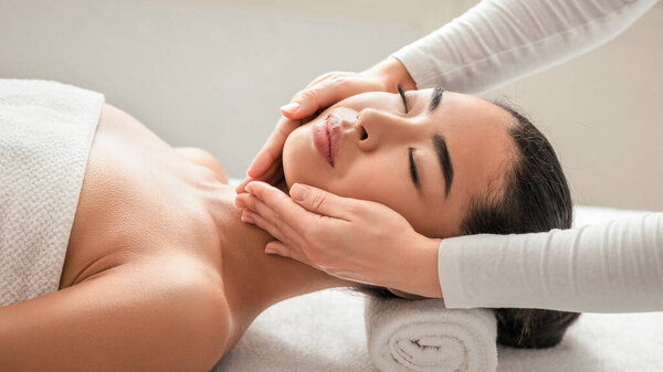 Facial beauty treatment. Relaxed asian woman getting professional face lifting massage at cosmetology cabinet or beauty parlor, young korean lady having spa wellness day, closeup shot with free space