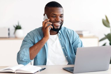 Uzaktan kumanda. İçişleri Bakanlığı 'nda cep telefonu ve dizüstü bilgisayar kullanan siyahi serbest çalışan, masada oturan, bilgisayarla uğraşan ve telefon konuşmasının keyfini çıkaran,