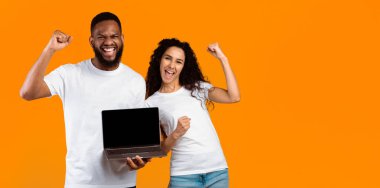 Çok Irklı Çift Laptop Boş Ekran Jesti Gösteriyor Evet Sarı Stüdyo Arkaplanının Üzerinde Duruyor. Erkek ve Kadın Bilgisayar Monitörü Gösteren Web Sitesi Tavsiye Ediyor. Mockup, Kopyalama Boşluğu Olan Panorama