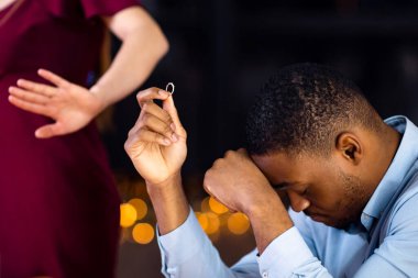 Başarısız Teklif Konsepti. Nişan yüzüğünü reddeden ve erkek arkadaşını, restoranda masada oturan, depresyonda ve yalnız hisseden çaresiz Afrikalı Amerikalı erkeği terk eden kadın.