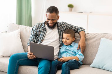 Black Daddy ve oğlu dizüstü bilgisayarda film izliyorlar koltukta oturuyorlar, hafta sonunu evde birlikte geçiriyorlar. Teknoloji ve Gadget 'lar, iki kişilik aile oturma odasında bilgisayar kullanıyor.