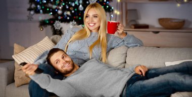 Mutlu evli genç bir çift televizyon izliyor, evdeki kanepede oturuyor, Noel arifesini birlikte geçiriyorlar, boş yer var. Neşeli genç bir kadın kahve içiyor, gülümsüyor, rahatlamış bir adam kucağında yatıyor.