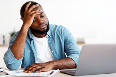 Stresli Siyah Erkek Girişimci 'nin iş yerinde sorunları var. Ofiste dizüstü bilgisayarla üzgün bir şekilde oturan ve umutsuzca kafasını okşayan depresif Afrikalı Amerikalı adam, boş alanla yakın çekim yaptı.