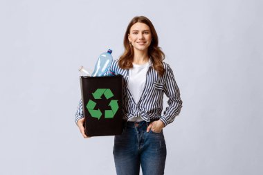 Sıfır Atık Kavramı. Elinde boş plastik şişeler olan, gülümseyen genç bir kadın, Milenyum kadınının geri dönüşüm için çöpleri ayırması, ışık stüdyosunun arka planında durması,