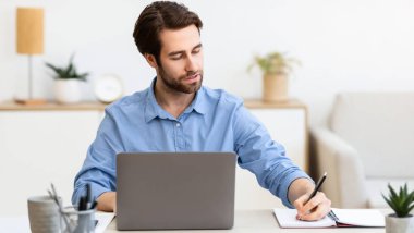 İş kariyeri. Modern ofiste oturan ve dizüstü bilgisayarda çalışan kendine güvenen girişimci not alıyor. İşadamı Pozisyonu İş yeri Konsepti. Seçici Odaklanma