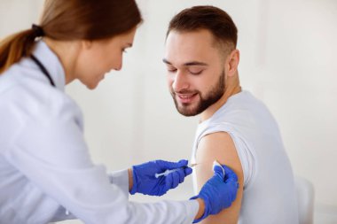 Kadın doktor, erkek hastaya klinikte koronavirüs aşısı yapıyor. Covid-19 aşı kampanyasına katılan genç adam. Sağlık ve Sağlık Hizmetleri kavramı