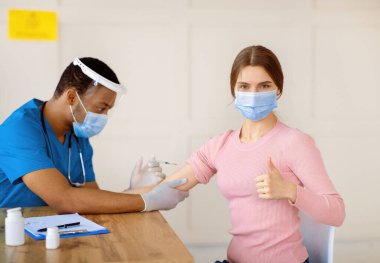 Milenyum bayanı koronavirüs aşısı yaptırıyor, baş parmağını kaldırıyor, sağlık merkezinde koromavirüs aşılanmasını onaylıyor. Viral hastalık tedavisi ve önleme kavramı