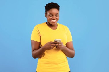 Gülümseyen Siyah Büyük Bayan Akıllı Telefon Mesajı Kullanıyor Mavi Stüdyo Arkaplanının Üzerinde Duruyor. Gezici Uygulama Kullanan Afrikalı Milenyum Kadını. Mutlu Kadın Telefon Kullanıcı Konsepti