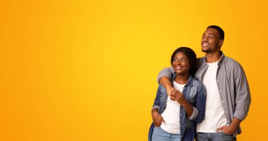 Güzel teklif. Genç, mutlu, siyah bir çift, fotokopi alanına ilgi ile bakıyor, neşeli bir milenyum erkeği ve kadını, sarı arka planda izole bir şekilde duruyor, kopya alanı olan bir manzara.