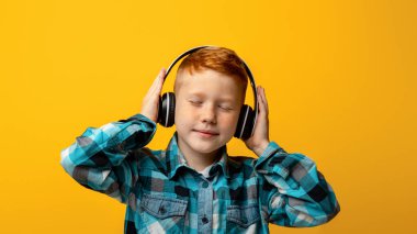 Kablosuz kulaklıklı neşeli kızıl saçlı çocuk müzik dinliyor, dans ediyor, sarı stüdyo arka planı, fotokopi odası. Çocuklar için eğlence ve yaşam tarzı konsepti