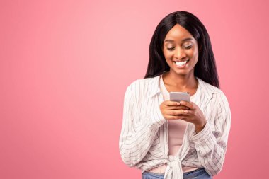 Pembe stüdyo arka planında akıllı telefondan internette sörf yapan güzel siyah bir kadın. Çevrimiçi çalışmalar ya da iş için mobil cihaz kullanan Afrikalı Amerikalı kadın, internet üzerinden arkadaşlarıyla iletişim kuruyor.