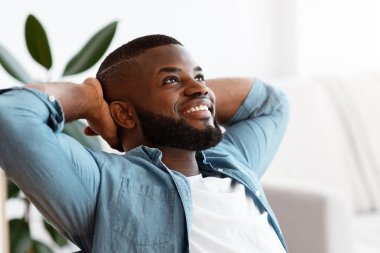 Uzak bir kariyer. Neşeli Afrikalı Amerikalı Serbest Çalışan Adam İçişleri Bakanlığı 'nda elleri arkada sırtüstü uzanıyor, gülümseyen siyah adam iş yerinde hayal gibi bir ifadeyle dinleniyor, boşluğu kopyalıyor.