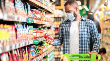 Market alışverişi. Marketten yiyecek alan Afrikalı Amerikalı adam koruyucu yüz maskesi takıyor, dükkânda arabasıyla duruyor. Erkek Alıcı Müşteri Seçme Ürünleri. Boşluğu Kopyala