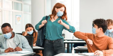 Virüs Kavramını yaymayı bırak. Birbirlerini selamlayan ve sınıfta dirsek tokuşturan koruyucu maskeler takan farklı sınıf arkadaşları. Sırt çantalı bir kadın, masada oturan bir adam.