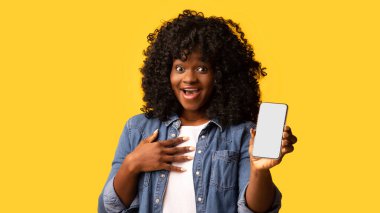 Modern akıllı telefonu boş ekranla gösteren genç siyahi kadın, güzel mobil uygulamalar, sarı stüdyo arka planı, kopyalama alanı kullandıktan sonra pozitif duygularını paylaşıyor.