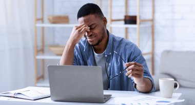 Modern ofiste bilgisayar başında oturan siyah adam göz yorgunluğu ve göz yorgunluğundan muzdarip. Burun köprüsüne masaj yapıyor. Göz görme problemi, baş ağrısı, glikoma semptomları