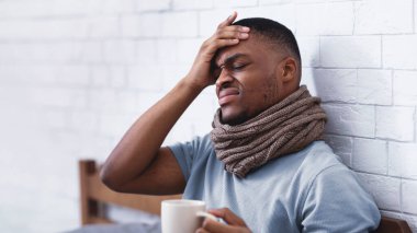 Hasta Afrikalı adam alnına dokunuyor, ateşi var ve baş ağrısı çekiyor. Evdeki yatak odasında yatıyor. Coronavirus ve Grip Belirtileri, Erkek Sağlık Sorunları Konsepti
