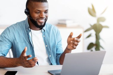 Uzaktan iletişim. Ofisteki bilgisayarla video görüşmesi yapan, laptop kamerasında konuşan, hareket eden, internetten konferans veren, interneti kopyalayan mutlu Afrikalı Amerikalı adam.