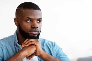 Ciddi bir yüz ifadesiyle oturan yakışıklı siyahi adamın yakın plan portresi, bir şeyler düşünen, ilham bekleyen, çenesini ellerine dayayan, uzayı kopyalayan, bir şeyler düşünen Afrikalı Amerikalı genç adam.