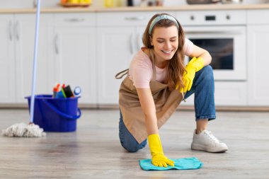 Profesyonel temizlik servisi. Önlüklü neşeli genç bayan ve modern mutfakta yerleri silen lastik eldivenler. Mutlu ev hizmetçisi portresi, temizlik, ev işleri.