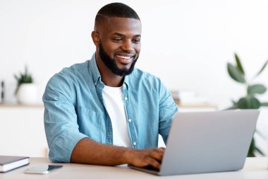 Uzaktan kumanda. İçişleri Bakanlığı 'nda dizüstü bilgisayarda çalışan yakışıklı ve serbest çalışan, bilgisayarla masasında oturan, ekranlara bakıp gülümseyen, serbest çalışmaktan hoşlanan, boşluğu kopyalayan siyahi bir adam.