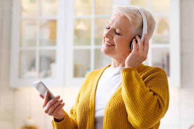 Neşeli büyükannem evde eğleniyor, cep telefonundan müzik dinliyor, fotokopi çekiyor. Akıllı telefon ve kablosuz kulaklıkta müzikal mobil uygulama kullanan gözleri kapalı son sınıf öğrencisi bir bayan.