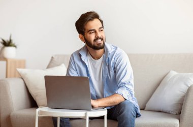 Evde dizüstü bilgisayarla çalışan ve başka tarafa bakan düşünceli bir Arap 'ın portresi iş fikirlerini düşünen, uzaktan çalışmaktan hoşlanan düşünceli bir doğulu adam, kopyalama alanı.
