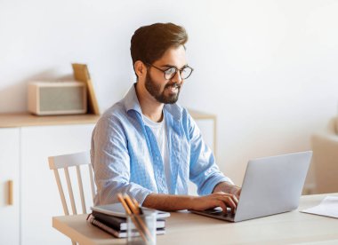 Milenyum Arap serbest çalışanı ev bilgisayarında dizüstü bilgisayarda çalışıyor, doğulu adam masa başında oturuyor bilgisayar ekranına bakıyor ve klavyede daktilo yazıyor, uzak iş fırsatlarının tadını çıkarıyor, boşluğu kopyalıyor.