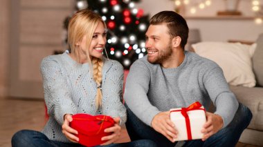 Mutlu erkek ve kadın Noel hediyelerini tutuyor ve birbirlerine bakıyorlar, evde birlikte Noel 'i kutluyorlar.