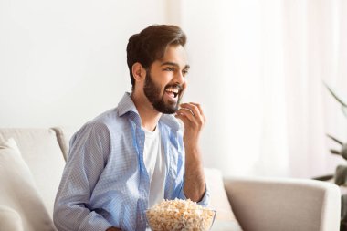 Neşeli doğulu adam evde boş vakit geçiriyor, televizyon izliyor ve patlamış mısır yiyor. Mutlu Arap adam oturma odasında kanepede dinlenirken komedi filminden zevk alıyor.