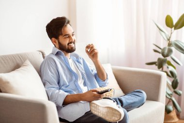 Evde TV izliyordum. Neşeli Arap adam kanepede dinleniyor ve patlamış mısır yiyor, milenyum doğusundan gülümsüyor favori televizyon programının tadını çıkarıyor, ev işleri yapıyor, uzay kopyaları yapıyor.