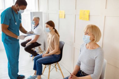 Erkek doktor genç bir bayanla konuşuyor, klinik bekleme odasında covid-19 aşısından önce not alıyor. Coronavirus bağışıklığı, küresel virüs kampanyasına karşı koruma