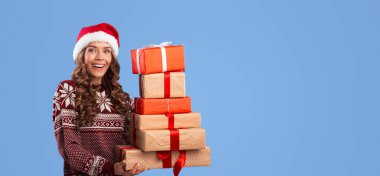 Noel Baba şapkalı mutlu milenyum hanımefendileri mavi arka planda kocaman Noel hediyeleri taşıyor, panorama