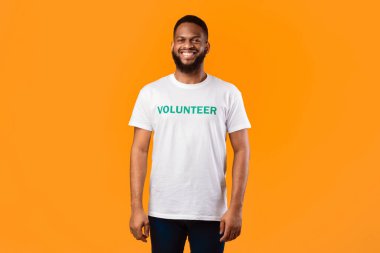 Mutlu Siyah Gönüllü Adam, kameraya gülümsüyor ve sarı arka planda yazılı forma giyiyor. Stüdyoda aktivist pozu. Gönüllü Kariyer Konsepti