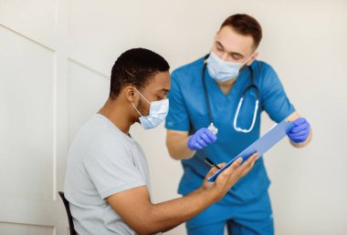 Afro-Amerikalı erkek hasta hastanede koronavirüs aşısı yapılmadan önce evrakları imzalıyor. Siyahi adam klinikte covid-19 aşılamasına belgelenmiş anlaşma yapıyor.