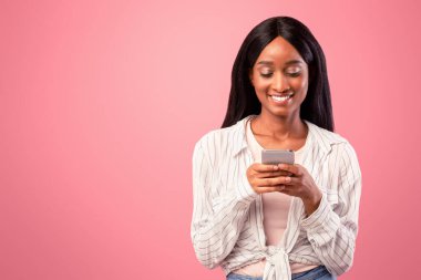 Çevrimiçi yaşam konsepti. Pembe stüdyo arka planında akıllı telefon kullanan çekici siyahi kadın. Güzel Afrikalı Amerikalı kadın internette geziniyor, mesaj gönderiyor, arkadaşlarıyla sohbet ediyor, sosyal medyayı kontrol ediyor.