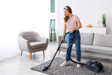 Neşeli kadın temizlikçi, elektrikli süpürgeyle evi temizliyor, uzun bir portre. Pozitif genç kadın ev işleri yapıyor, evini temiz tutuyor. Ev hijyeni kavramı