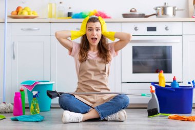 Dehşete düşmüş genç bir kadının uzun bir portresi. Başını tutuyor ve ev işlerinden bağırıyor. Mutfakta yerde oturuyor, etrafı temizlik malzemeleriyle çevrili.