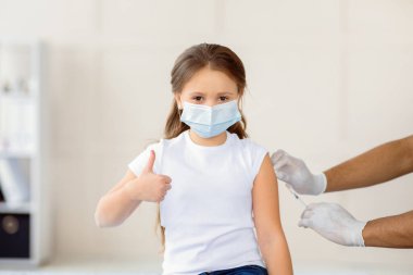 Başarılı koronavirüs aşısı. Hastanede covid-19 aşısı yapılırken küçük kız el hareketi yapıyor. Virüs ve nüfus aşılama kavramına karşı koruma