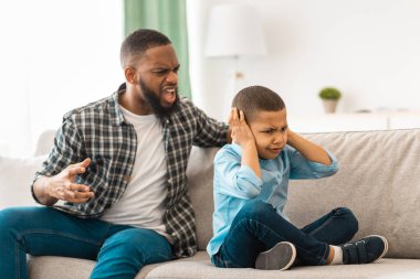 Saldırgan siyah baba, mutsuz çocuğa bağırıyor. Evdeki koltukta oturan çocuk kızıyor. Mutsuz çocukluk. Öfkeli baba ona bağırırken, Afrikalı küçük çocuk kulaklarını kapatıyordu. Aile İçi Şiddet