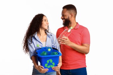 Atık ayıklama. Beyaz arka planda duran kullanılmış plastik şişelerle dolu geri dönüşüm sembollü çöp kutusunu düzenleyen çok kültürlü aile çifti. Stüdyo çekimi. Çöp İmha Konsepti