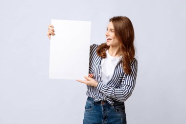 Elinde boş beyaz levhayla bekleyen genç bir kadın, teklif ya da ilanınız için boş bir afiş tutan, arka planda duran,